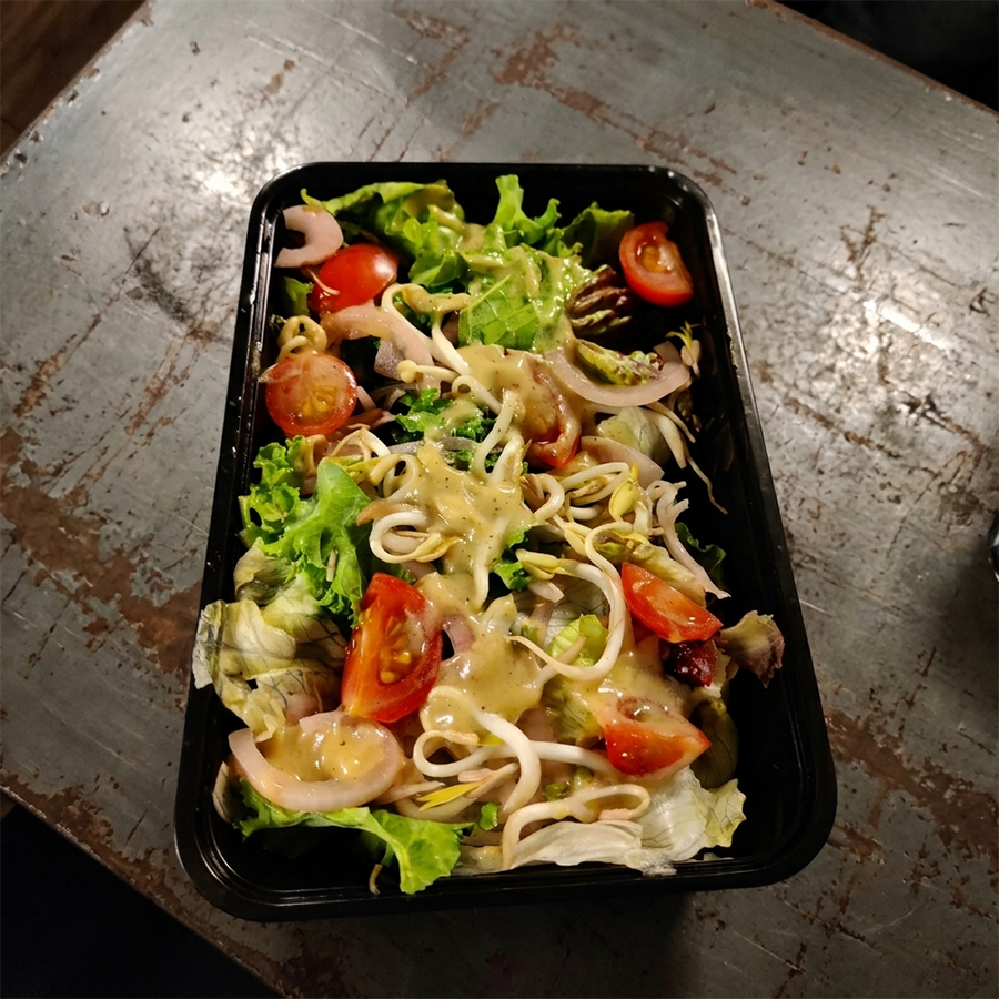 Fresh garden salad with cherry tomatoes, crisp lettuce, and sprouts in a black container