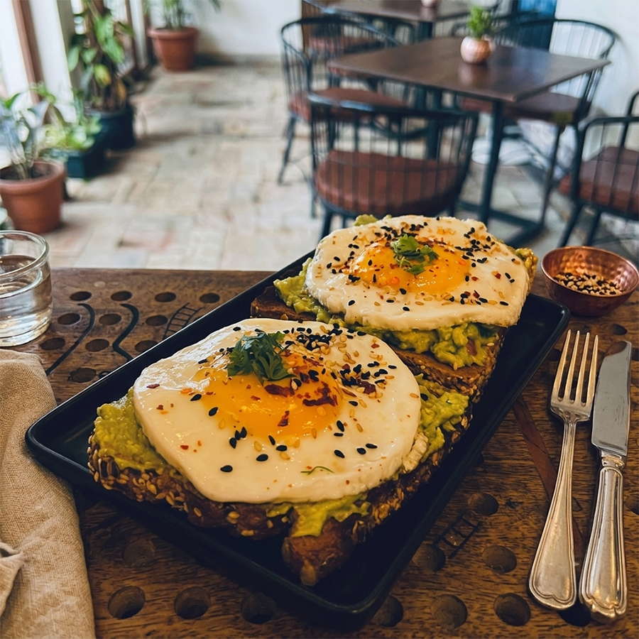 Multigrain toast topped with smashed avocado, fried eggs, and toasted seeds.